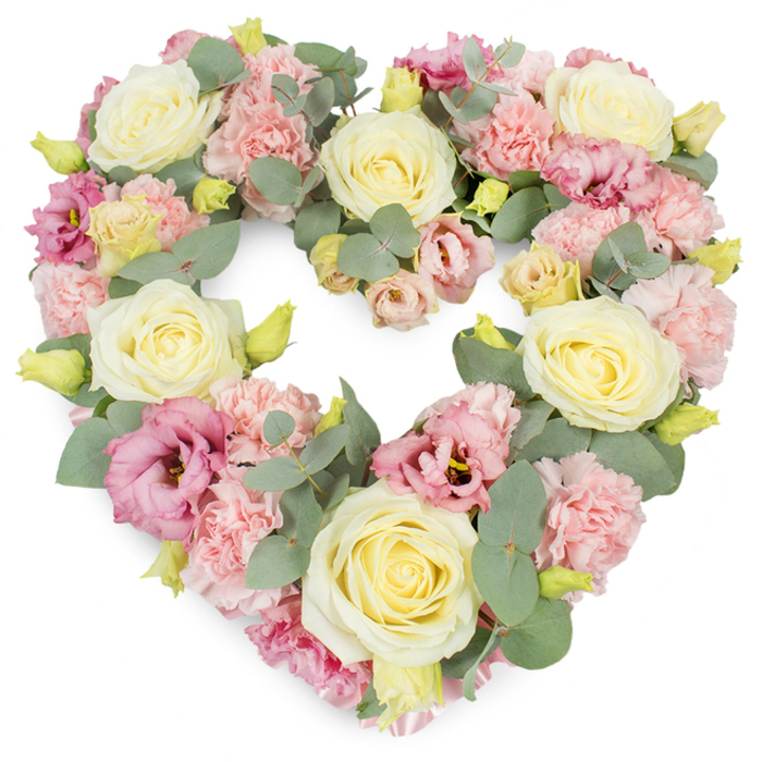 A meticulously crafted heart-shaped floral wreath appears against a bright white background, every petal carefully placed to form a seamless symbol of love and remembrance. The heart is generously filled from edge to edge, leaving no empty spaces, only layers of pastel flowers that seem to gently embrace one another. Creamy yellow and ivory roses form the anchor of the design, their blooms opened to a luxurious fullness, each petal curving softly over the next in a tight, elegant spiral. Nestled around these roses are clusters of pastel pink carnations, their finely frilled petals creating a soft, cushion-like texture that brings an almost tactile sense of comfort. Woven throughout are deeper pink and mauve lisianthus flowers, adding a slightly richer hue that draws the eye inward, their open, bell-shaped blossoms and delicate, curling edges introducing both movement and grace. Silvery-green eucalyptus foliage threads through the arrangement, its rounded leaves and cool tones offering a calm backdrop to the warm creams and pinks, and subtly emphasizing the clean heart outline. Small yellow-green buds are visible at different depths within the design, hinting at freshness and the promise of life even in moments of mourning. The overall mood is peaceful and reflective, ideal for a funeral, graveside tribute, or memorial service for families in and around Leamouth. It evokes the quiet stillness of the nearby riverside paths, a floral gesture that feels deeply personal and respectful, as if created to hold cherished memories close in a soft, pastel embrace.