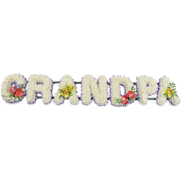 In this thoughtfully crafted funeral display, the word "GRANDPA" stretches horizontally in seven sturdy block capital letters, each one formed from a dense bed of small white chrysanthemum blooms. The flowers are placed so precisely that they resemble soft, snow-white cushions, every tiny petal contributing to a sense of purity, serenity, and loving care. A fine trim of light lavender ribbon encircles the base of each letter, just visible beneath the blooms, adding a whisper of pastel colour that gently outlines the shapes, making them clearly legible even from the back of a chapel in Leamouth. The letters are fixed to dark green bars that anchor the tribute as a single piece, ready to rest along the side of a coffin or on a stand at the front of a service. Splashes of colour are introduced through carefully positioned sprays: the "G" and the "D" are highlighted with dramatic red anthuriums, their waxy, heart-shaped petals and upright yellow spadices nestled among glossy green leaves and a scattering of tiny purple filler flowers, symbolising deep love and remembrance. The first and last "A"s are adorned with clusters of yellow-green orchids, whose delicate, arching petals and intricate centres lend a gentle brightness and sense of enduring affection for a much-loved grandfather. The overall impression is one of quiet elegance and heartfelt respect, a bespoke floral tribute of the kind often chosen for funerals, wakes, or graveside tributes around Leamouth. It reflects the steady hands and local experience of florists who understand how to weave comfort, memory, and beauty into a single, meaningful arrangement.