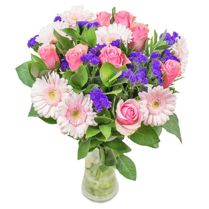 A vibrant, elegantly arranged bouquet sits in a crystal-clear glass vase, illuminated by soft daylight that hints at a Leamouth studio overlooking the Thames. In the heart of this arrangement, approximately 7-9 velvety pink roses take centre stage-many petals tightly coiled in the classic spiral, with others just beginning to unfurl. These are thoughtfully paired with about 5-7 pale pink gerbera daisies, identifiable by their generously radiant, sun-like faces and nearly white centres, echoing the gentle palette found in local community gardens. Punctuating the softness, clusters of bright purple statice bring unexpected energy, their textural charm contrasting with the smoothness of the rose petals. Lush, dark green foliage frames each bloom, imparting a rich freshness that recalls the open green spaces of Limmo Peninsula. Through the transparent vase, the stems are visible-a visual testament to the bouquet's natural abundance and the care that goes into its curation. This arrangement invites feelings of joy, celebration, and affection, well-suited to birthdays, anniversaries, or an exuberant 'thinking of you' delivered to homes and offices from Leamouth Florist throughout E14. Each floral choice is deliberate, creating a composition that is as refined as it is welcoming, easily brightening any riverside setting or workspace.